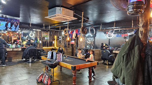 Interior de Barbería El Russo con sillones, mesa de pool y clientes