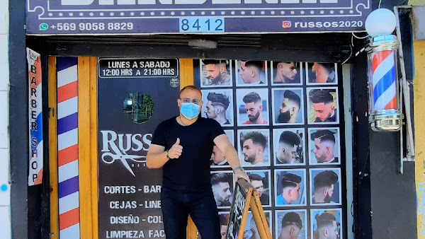Fachada de Russos Barbería con poste de barbero y afiche de cortes