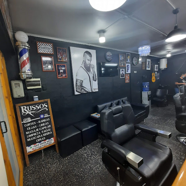 Interior de Russos Barbería con sillón, poste y pizarra de servicios